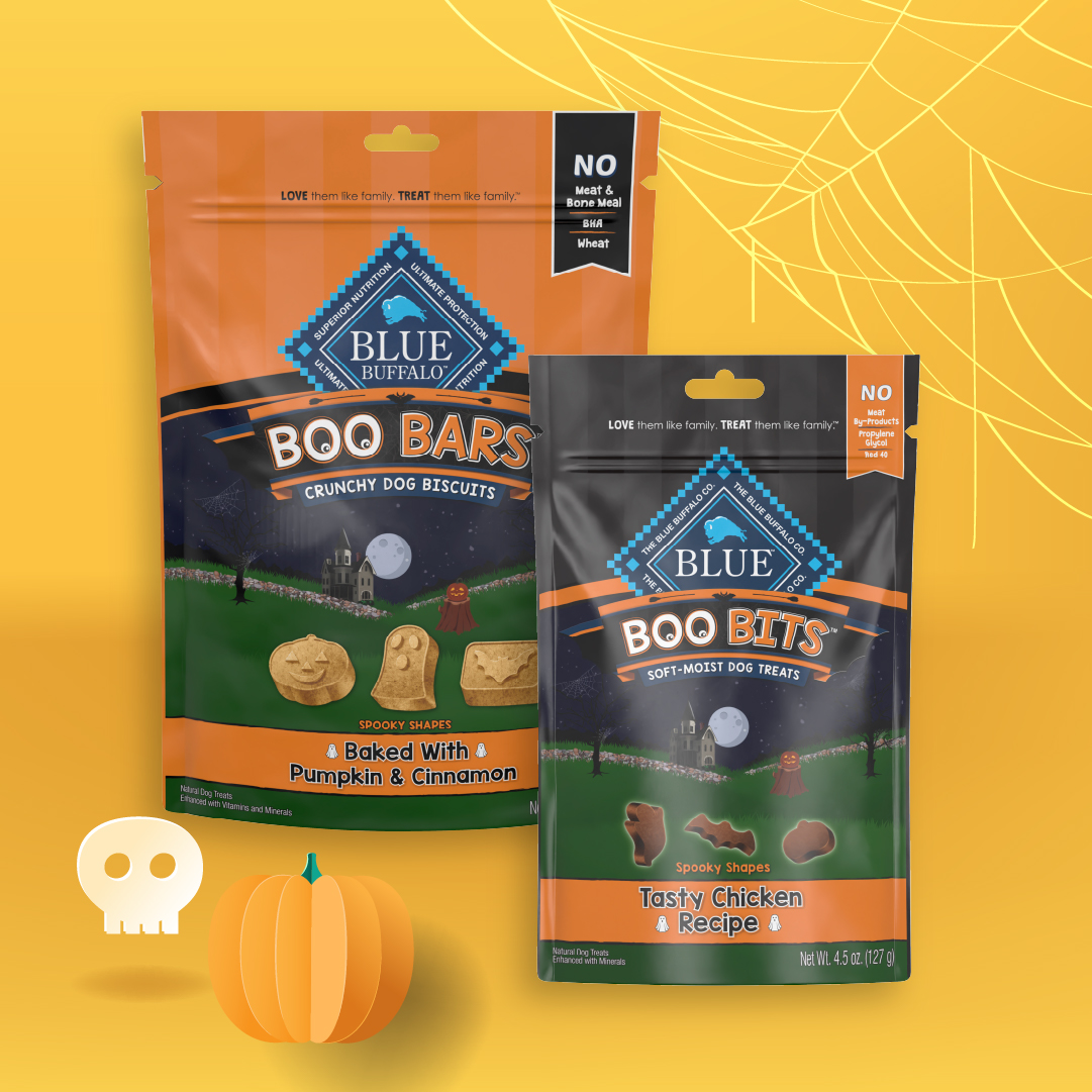 Two pouches of Blue Buffalo Halloween treats for dogs displayed on a yellow background with spider web, skull, and pumpkin illustrations.